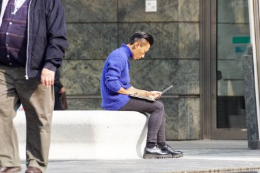 Milan, İtalya 4 Mayıs 2019: Kentin meydanındaki bankta otururken bilgisayar kullanan genç adam