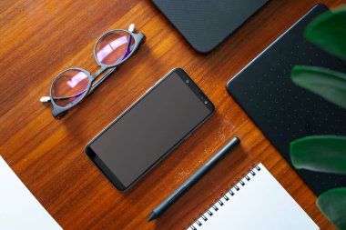 Ofis masasının üstünde güneş gözlüklü telefon ve defter var.