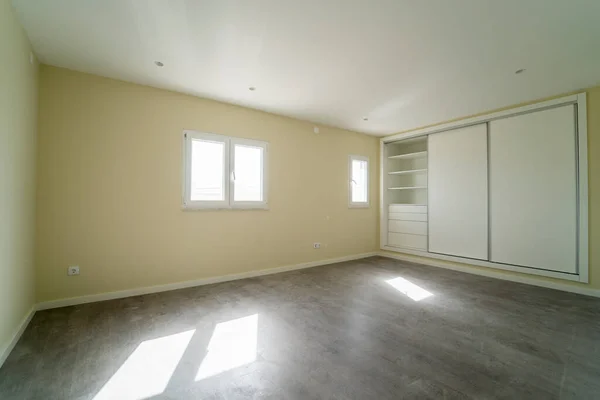 Empty room with dark wooden floating laminate flooring and wardrobe. House interior, wide bedroom space. Newly recently painted new apartment or house. Wood floor. Real state and property management
