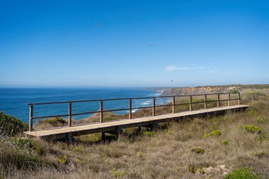 Uçurumun tepesinde boş ahşap geçit var. Okyanus kıyısındaki tahta köprü. Yürüyüş rotası, rota. Deniz manzarası ya da deniz manzarası. Deniz manzarası. Tatil, tatil, yaz tatili.