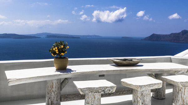 Живописный пейзаж острова Санторини с апельсиновым деревом на большом деревянном столе. С террасы открывается потрясающий вид на Кальдеру древнего вулкана
.