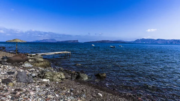 Santorini Adası üzerinde kayalık Akdeniz kıyısında deniz rüzgar şemsiye güneş ve eski dalgalı footway kırıldı.