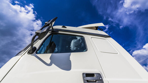 White cumulus clouds in the blue sky are reflected in the side windows and rear-view mirrors of a large truck.