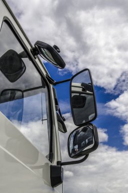 Mavi gökyüzünde beyaz kümülüs bulutlar yan camlar ve büyük bir kamyonun arka - aynaları yansır.