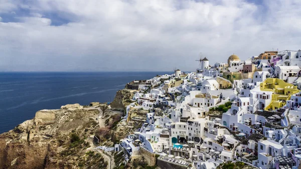 The morning landscape of the streets of Oia on the island of Santorini is a bright color picture. Small houses clung to the rocky shore of the island, and windmills remind that over the island strong winds blow.