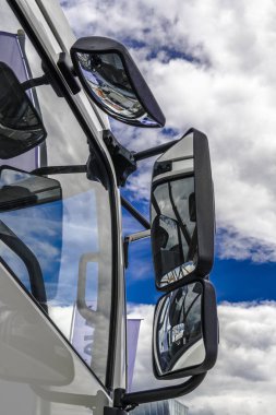 Mavi gökyüzünde beyaz kümülüs bulutlar yan camlar ve büyük bir kamyonun arka - aynaları yansır.