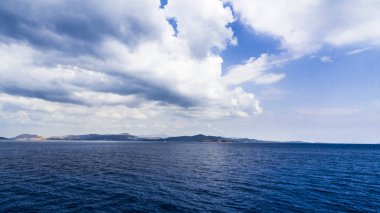 Ege Denizi'nin dağlık kıyısında fırtına bulutları ile kaplıdır ve koyu mavi derin kıyı suları vardır.