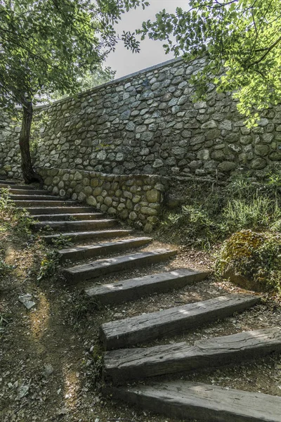 The dilapidated wooden steps of the old staircase lead past the ancient stone wall under the thick branches of trees to the top of the mountain, where the Greek Orthodox monastery is located.
