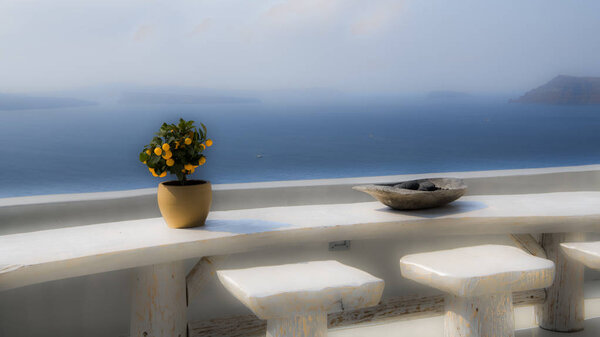 Живописный пейзаж острова Санторини с апельсиновым деревом на большом деревянном столе. С террасы открывается потрясающий вид на Кальдеру древнего вулкана
.