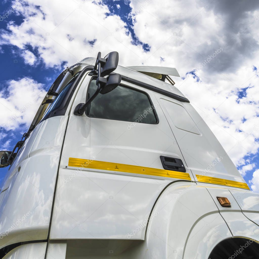 White cumulus clouds in the blue sky are reflected in the side windows and rear-view mirrors of a large truck.