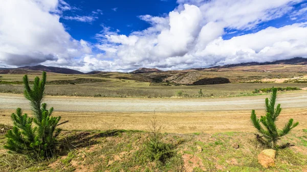 The dirt road runs along the mountain plateau in the Andes at an altitude of 3.500 meters between the mountain peaks covered with snow.