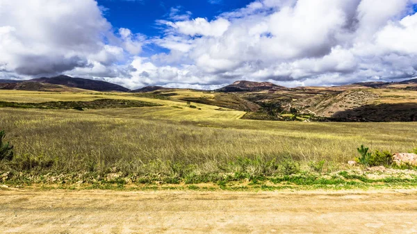 The dirt road runs along the mountain plateau in the Andes at an altitude of 3.500 meters between the mountain peaks covered with snow.