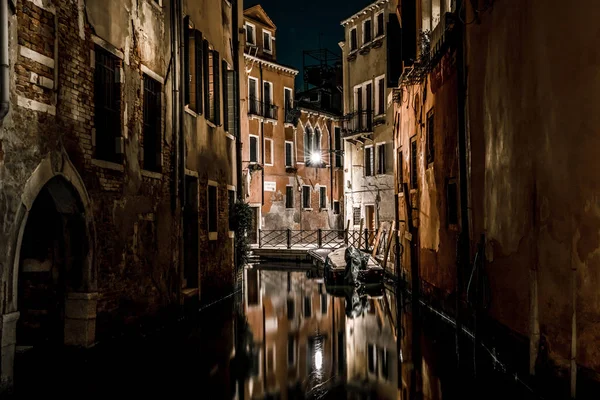 Poorly lit houses stand along the dark Venetian canal. The walls of the boats tied houses of local residents.