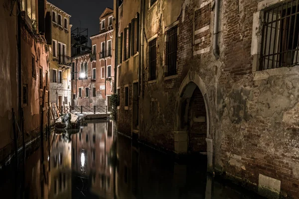 Poorly lit houses stand along the dark Venetian canal. The walls of the boats tied houses of local residents.