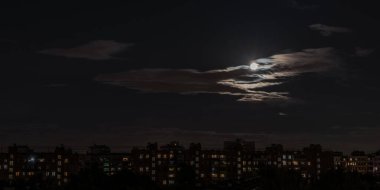 Dolunay, kısmen bulutlarla kaplı, büyük bir şehrin gece konutlarını aydınlatır.