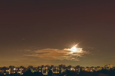 Dolunay, kısmen bulutlarla kaplı, büyük bir şehrin gece konutlarını aydınlatır.