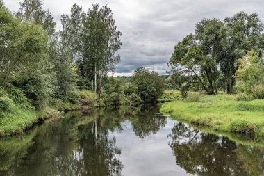 Fırtına bulutları Moskova yakınlarındaki sakin bir nehre yansıyor, yeşil çayırlar boyunca akıyor..