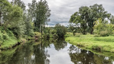 Fırtına bulutları Moskova yakınlarındaki sakin bir nehre yansıyor, yeşil çayırlar boyunca akıyor..
