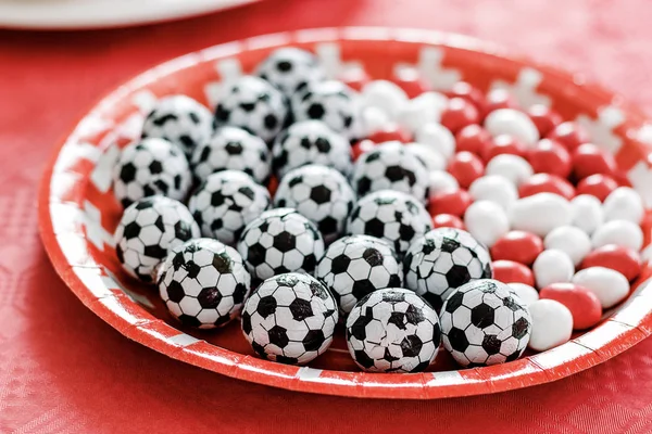 Doughnuts and chocolate candy im football theme on red table cloth. Swiss flag red and white cross, football in Switzerland. Football party at home with snacks and sweets. Football fever worldwide.