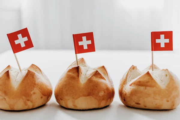 Traditional swiss bread buns called in German 1.Augustweggen baked in Switzerland to celebrate Swiss National Day on August 1st. The top of the bread being cut crosswise to shape a cross as symbol of Switzerland. Swiss flags on wooden toothpicks.  Wh