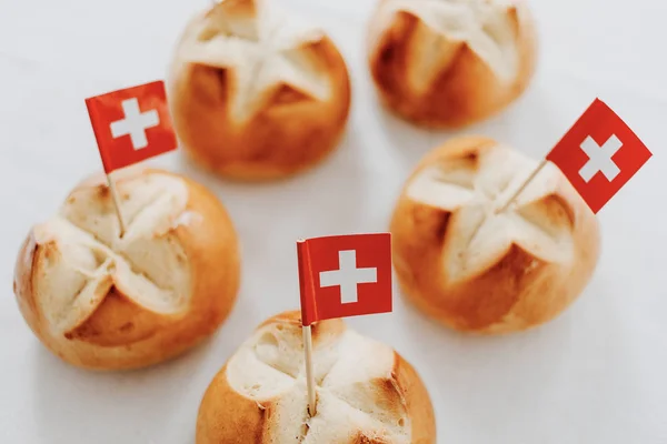 Traditional swiss bread buns called in German 1.Augustweggen baked in Switzerland to celebrate Swiss National Day on August 1st. The top of the bread being cut crosswise to shape a cross as symbol of Switzerland. Swiss flags on wooden toothpicks.  Wh