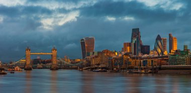 London, England - Panoramic skyline view of London with Tower Bridge, skyscrapers of Bank District and other landmarks at golden hour sunrise. Dramatic dark clouds at background clipart