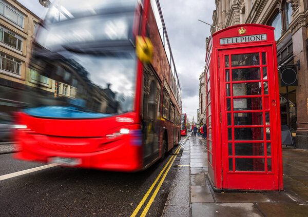 London, England - Iconic blurred red double-decker bus on the move with traditional red telephone box in the center of London at daytime