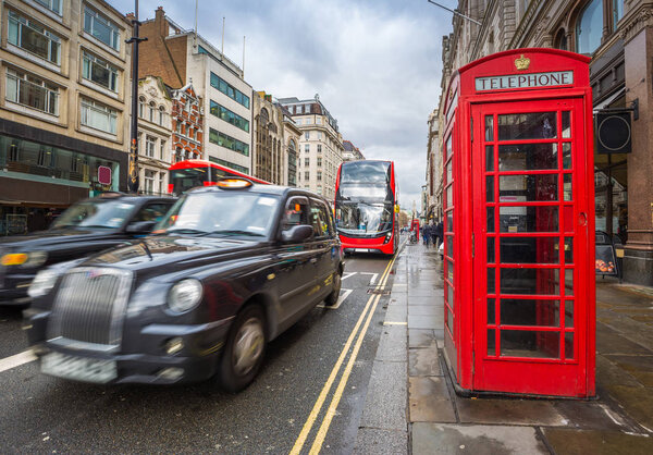 London, England - Iconic blurred black londoner taxies and red double-decker buses on the move with traditional red telephone box in the center of London at daytime