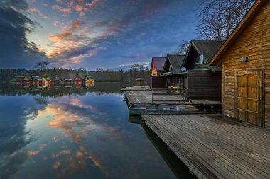 Tata, Hungary - Beautiful sunset over lake Derito (Derito to) in November with wooden fishing cottages and colourful sky and clouds clipart