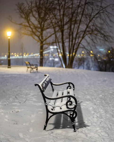 Budapest, Hungary - Two benches and lamp post in a snowy park at Buda district with Szechenyi Chain Bridge at background during heavy snowing at winter time