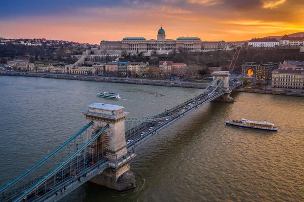 Будапешт, Венгрия - Воздушный вид на Цепной мост Фечаний и Королевский дворец Буда с красивым золотым закатом и прогулочными лодками на реке Дунай Стоковое Фото