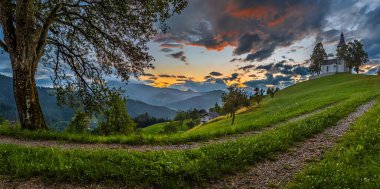 Skofja Loka, Slovenya - Sloven Alpleri 'nin büyüleyici tepelik kilisesi Sveti Tomaz (Saint Thomas), renkli gökyüzü ve yazın arka planda Julian Alps ile güzel panoramik kırsal manzarası