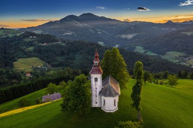 Skofja Loka, Slovenya - Muhteşem bir altın gün batımı, mavi gökyüzü ve yazın arka planda Julian Alps ile güzel tepe Sveti Tomaz (Saint Thomas) Kilisesi 'nin havadan görünüşü