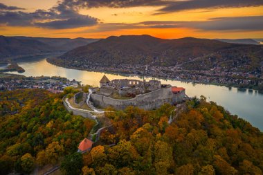 Visegrad, Macaristan - Sonbahar yaprakları ve ağaçlarıyla güzel yüksek Visegrad şatosunun insansız hava aracı görüntüsü. Dunakanyar ve arka planda altın gün batımı