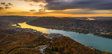 Visegrad, Macaristan - Sonbahar yaprakları ve ağaçlarıyla güzel yüksek Visegrad ve Salamon kalesinin hava panoramik drone görüntüsü. Dunakanyar ve arkada dramatik altın gün batımı