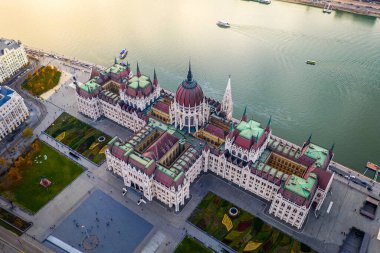 Budapest, Hungary - Aerial drone view of the beautiful Parliament of Hungary at sunset with golden lights on River Danube, sightseeing boats and traditional yellow tram clipart