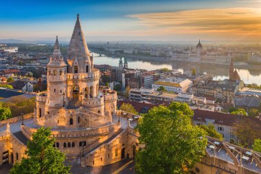 Budapeşte, Macaristan - Balıkçı Kalesi ve yeşil ağaçlarla güzel bir altın yaz gündoğumu. Arka planda Macaristan Parlamentosu ve Tuna Nehri var. Mavi gökyüzü.