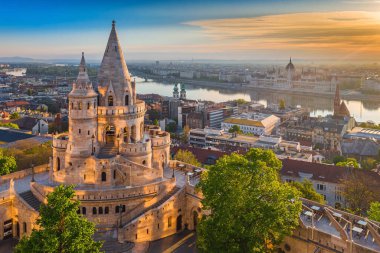Budapeşte, Macaristan - Balıkçı Kalesi ve yeşil ağaçlarla güzel bir altın yaz gündoğumu. Arka planda Macaristan Parlamentosu ve Tuna Nehri var. Mavi gökyüzü.