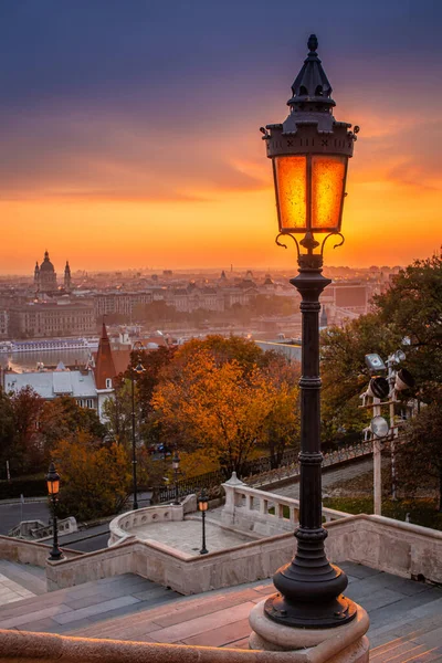 Budapest, Hungary - Colorful autumn morning at Budapest. Street lamp at the Fisherman\'s Bastion, St. Stephen\'s Basilica and amazing golden sunrise at the background with autumn foliage and trees
