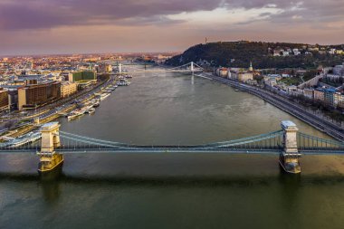 Budapeşte, Macaristan - Elisabeth Köprüsü, Hisar ve arkaplanda renkli gökyüzü ile günbatımında tamamen boş Szechenyi Zinciri Köprüsü 'nün havadan görünüşü. Coronavirüs salgını nedeniyle köprüde trafik yok.