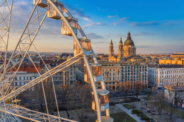 Budapest, Hungary - Aerial view of the ferris wheel at Elisabeth Square (Erzsebet ter) at sunset with warm colors, St. Stephen's Basilica and blue sky at background