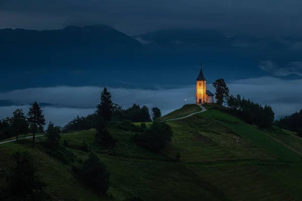 詹姆尼克 斯洛文尼亚 蓝色的时刻在詹姆尼克与照明圣普里莫兹山顶教堂在一个雾蒙蒙的夏日黎明 Julian Alps的背景 — 图库照片