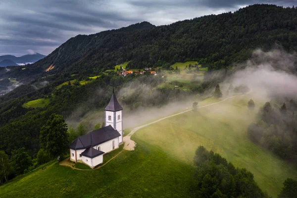 Jamnik Slovenia 在Jamnik Primoz教堂从空中俯瞰一个雾蒙蒙的夏日日出 雾气轻柔地弥漫在有五彩斑斓的天空和背景的朱利安阿尔卑斯山的小教堂周围 — 图库照片