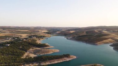 4K insansız hava aracı, yumuşak ışıkta nehir ve tarlaları yakalıyor. Kırsal arazide huzurlu bir gün batımı