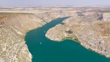 Drone, derin su ve kayaların üzerinde süzülen bir tekne gösteriyor..