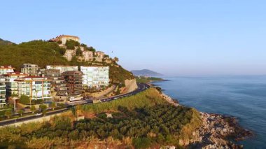 Taş sahili ve yeşil tarlaları olan bir otel kompleksi.