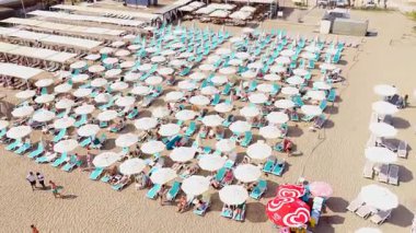 Açık mavi sularda yüzen insanlarla güneşli kıyı şeridi.