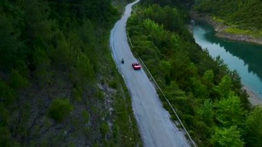 Nehir yolu ve köprünün yanında üstü açık kırmızı araçlar.