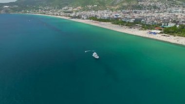 Beyaz teknenin kumlu kıyı şeridinin yanından geçerken üst görüntüsü.