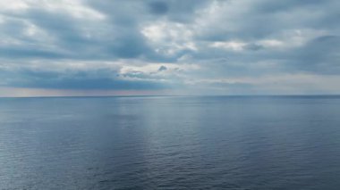 Bulutlu gökyüzünün altında sakin kıyı şeridinin yüksek hava görüntüsü.